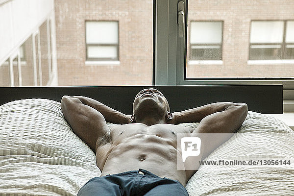 Shirtless man looking away while lying on bed at home