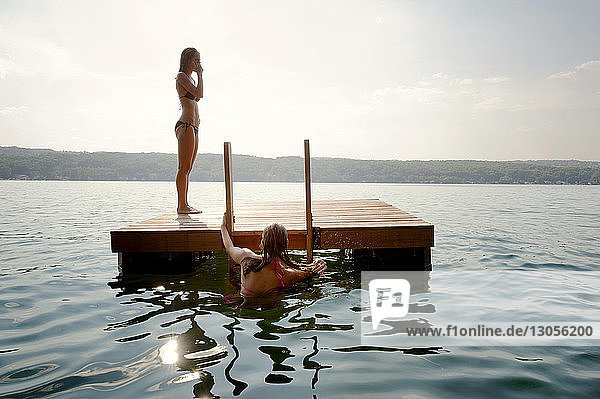 Freunde auf schwimmender Plattform im See gegen den Himmel an einem sonnigen Tag