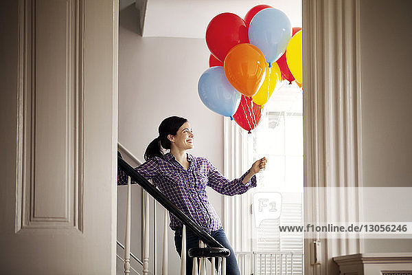 Glückliche Frau steht an der Treppe und hält Heliumballons