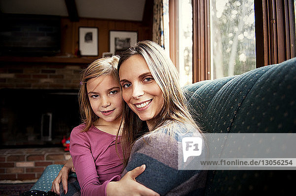 Porträt einer glücklichen Mutter  die ihre Tochter zu Hause auf dem Sofa umarmt