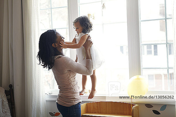 Mutter trägt Tochter  während sie zu Hause am Fenster steht
