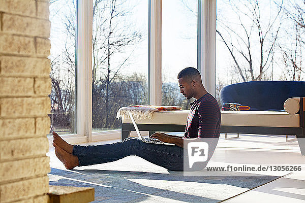 Mann benutzt Laptop  während er zu Hause auf dem Boden sitzt