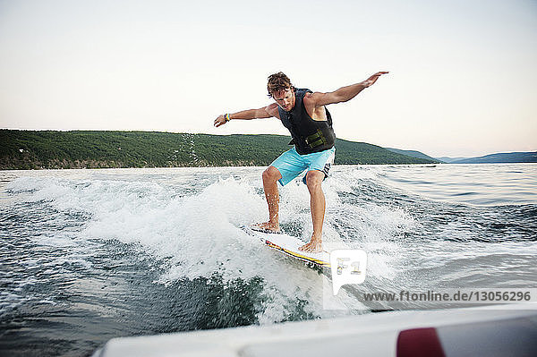Young man wake surfing in lake against clear sky