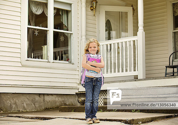 Porträt eines glücklichen Mädchens  das Bücher hält  während es vor dem Haus steht