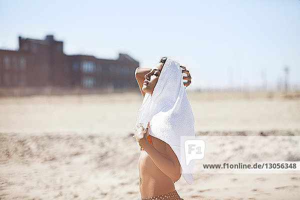 Woman with towel on head standing at beach against sky
