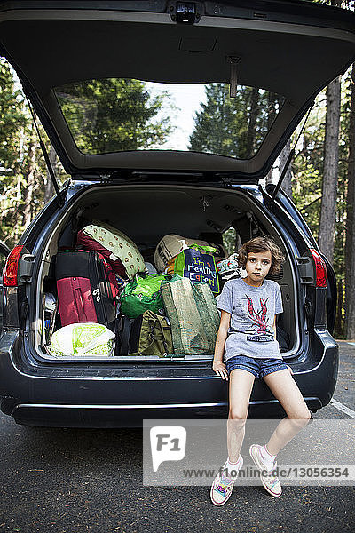Porträt eines Mädchens  das auf einem Kofferraum auf der Straße sitzt