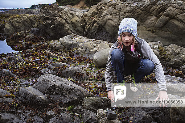 Portrait of girl crouching on rocks at beach