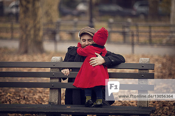 Vater umarmt auf Bank stehendes kleines Mädchen
