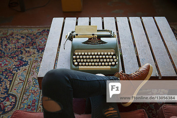 Beschnittenes Bild einer Frau  die zu Hause mit der Schreibmaschine auf einem Stuhl sitzt