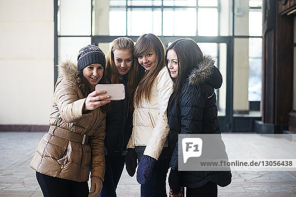 Freundinnen  die vor dem Gebäude stehen und sich per Smartphone selbstständig machen