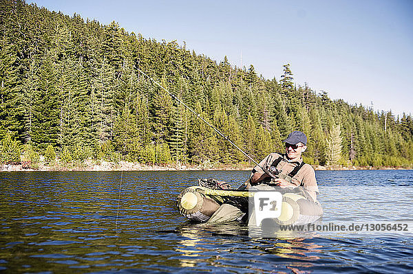 Happy man fishing while sitting on pontoon boat in lake