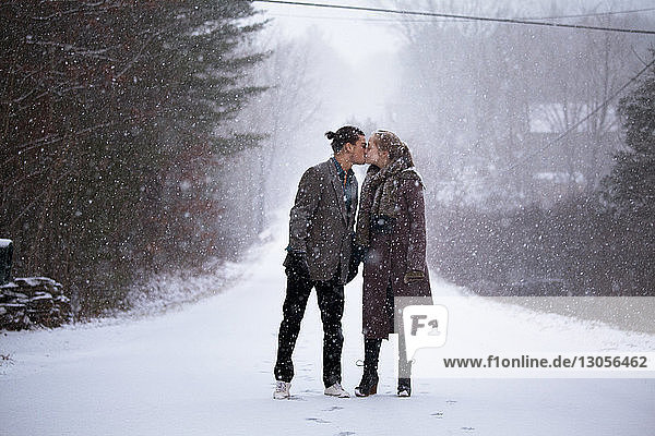 Romantic couple kissing while standing on snowy field during snowfall