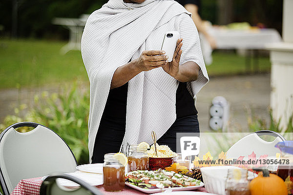 Mitschnitt einer Frau  die am Tisch stehend am Telefon Essen fotografiert