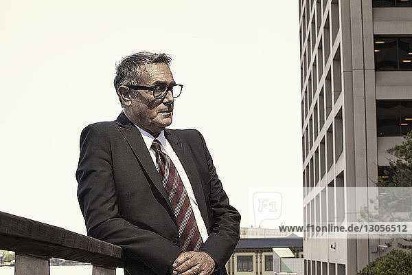 Businessman leaning on railing against clear sky