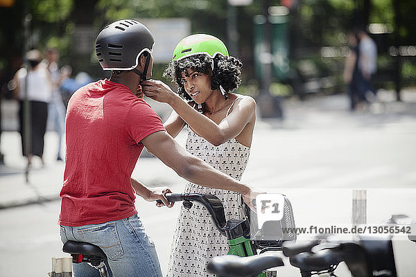 Woman fastening cycling helmet of man