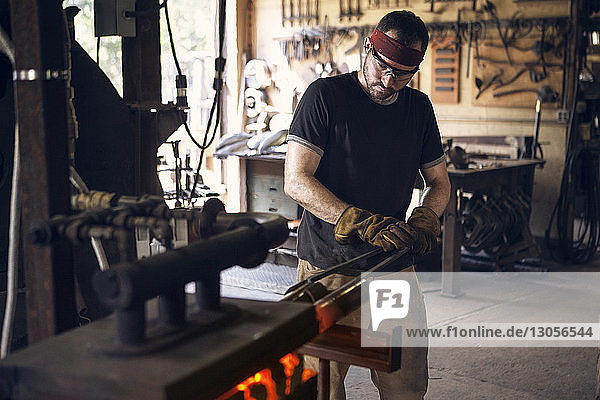 Blacksmith holding rod with tongs while forging in furnace at workshop