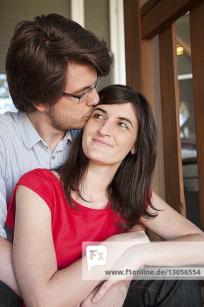 Mann küsst Freundin  während er am Geländer sitzt