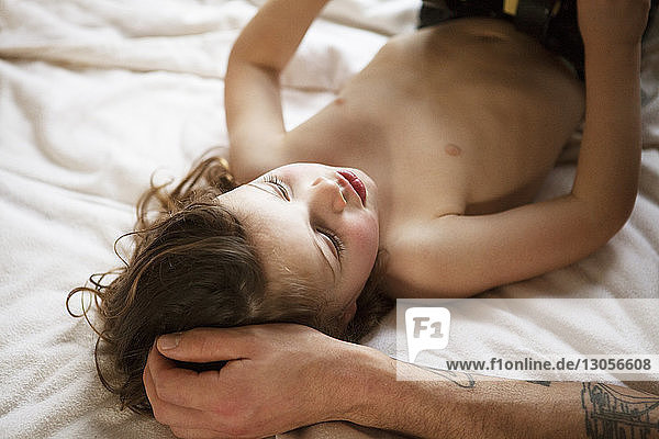 Ausgeschnittenes Bild einer Hand  die das Haar des Sohnes berührt  während er zu Hause auf dem Bett liegt