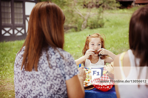 Mädchen isst Essen  während sie mit der Familie am Picknicktisch sitzt