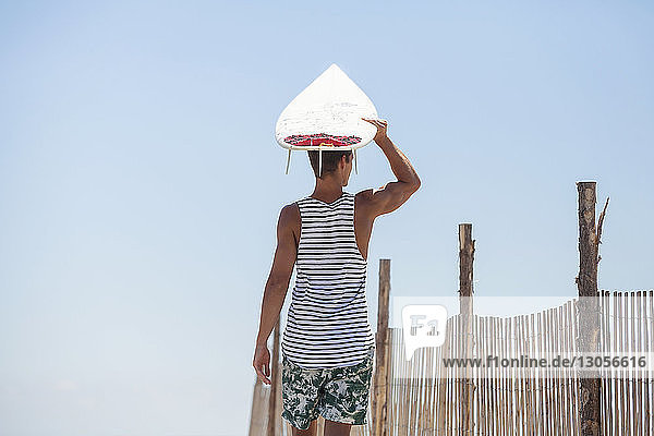 Mann trägt Surfbrett auf dem Kopf  während er am Strand steht