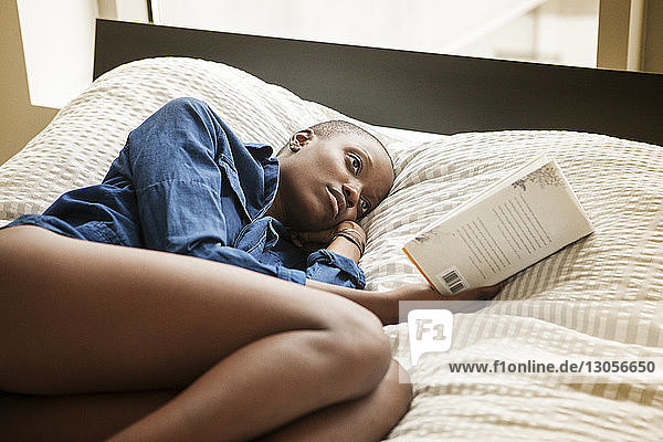 Woman reading book while lying on bed at home