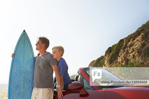 Vater und Sohn mit Surfbrett mit dem Auto gegen den Himmel