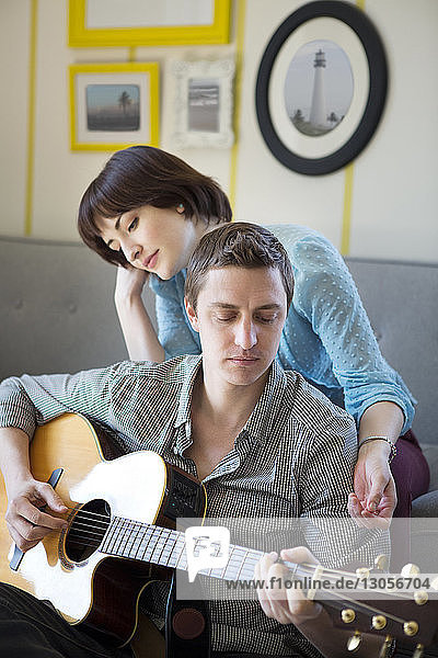 Frau hört zu Hause ihrem Freund beim Gitarrespielen zu