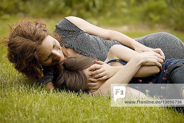 Mother looking at girl covering face with hands while lying on field