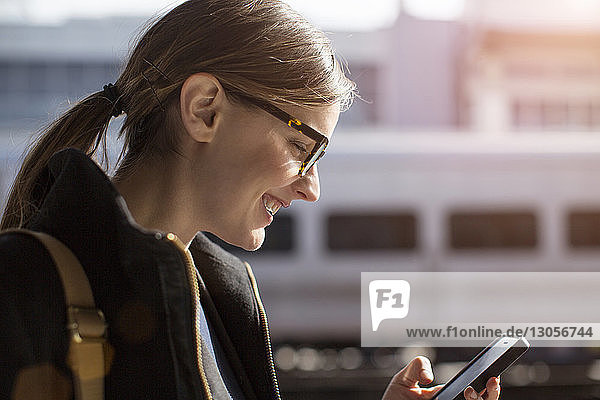 Side view of happy businesswoman using phone at railroad station