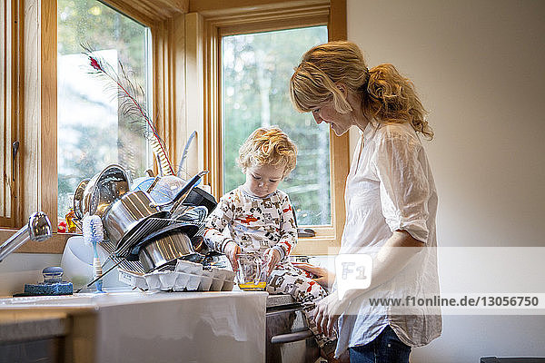Boy sitting on kitchen worktop by mother at home