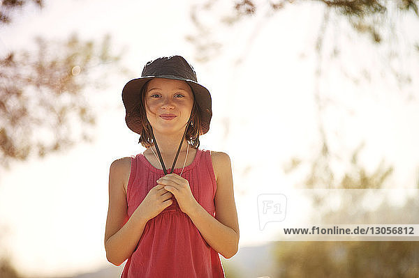 Portrait of happy girl in hat standing against sky on sunny day