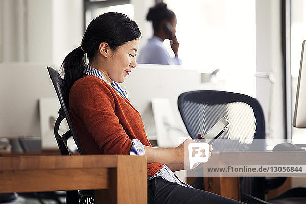 Geschäftsfrau benutzt Tablett  während sie im Büro auf einem Stuhl sitzt