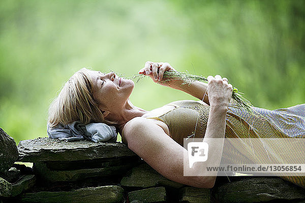 Woman playing with grass while lying on stone wall