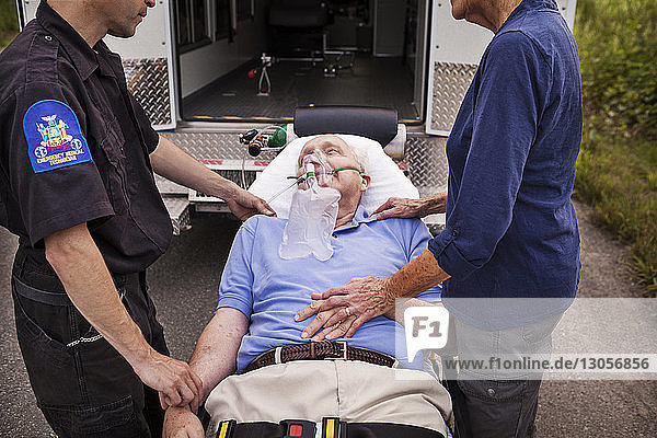 Ausgeschnittenes Bild eines Sanitäters und einer Frau  die auf einer Krankenhausbahre liegend beim Patienten stehen