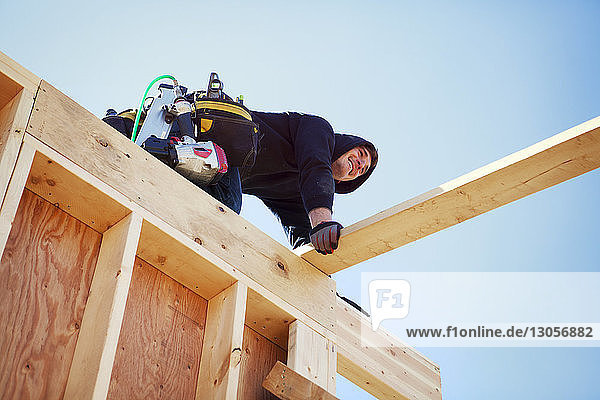 Niedrig-Winkel-Ansicht eines lächelnden Arbeiters  der vor blauem Himmel ein Baugerüst herstellt