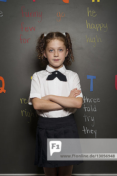 Portrait of confident schoolgirl standing against blackboard