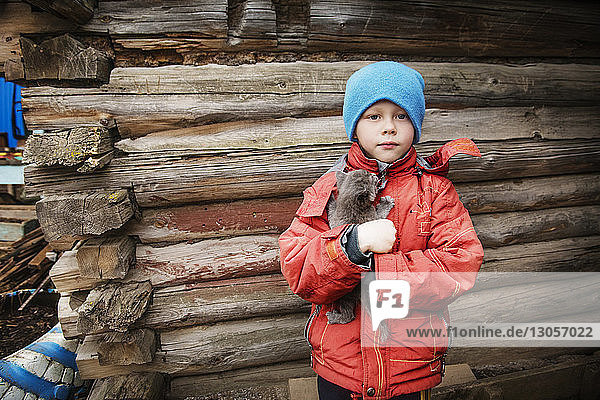 Portrait of boy carrying cat while standing against wooden wall