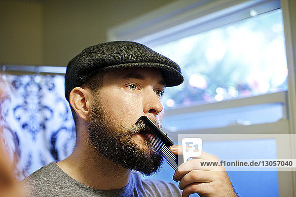 Man combing mustache while looking away at home