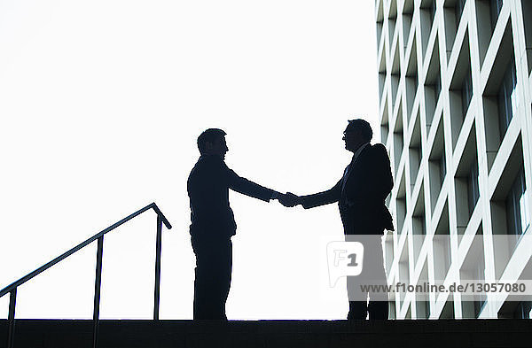 Silhouette of businessmen shaking hands against sky