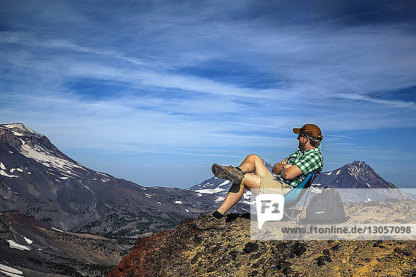 Hiker sitting on top of mountains against sky