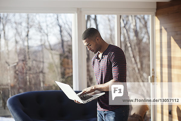 Mann benutzt Laptop-Computer  während er zu Hause steht