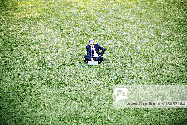 Businessman using laptop computer while sitting on grassy field