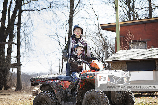 Portrait of boy sitting on quadbike while brother standing on field