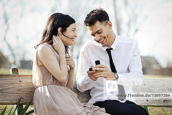 Glücklicher Mann zeigt Frau Schmuckkästchen  während er auf Bank sitzt