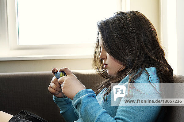 Seitenansicht eines Mädchens  das ein Mobiltelefon benutzt  während es sich zu Hause auf dem Sofa entspannt