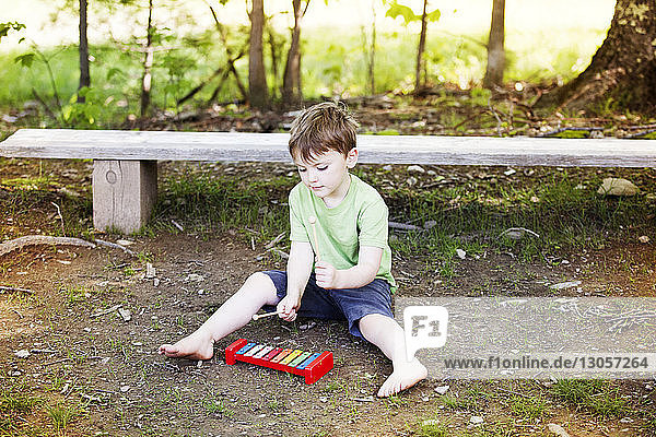 Hochwinkelansicht eines Jungen  der Spielzeug-Xylophon spielt  während er auf dem Spielplatz sitzt