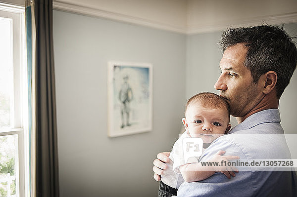Man looking away while carrying baby boy at home