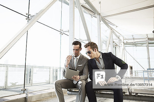 Geschäftsleute  die einen Tablet-Computer benutzen  während sie auf einer Bank sitzen