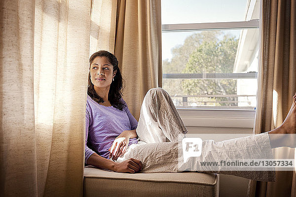 Nachdenkliche Frau sitzt zu Hause am Fenster