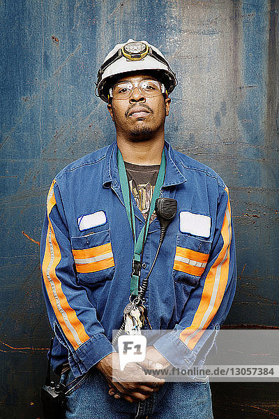 Porträt eines selbstbewussten männlichen Arbeiters,  der an einer Metallwand steht